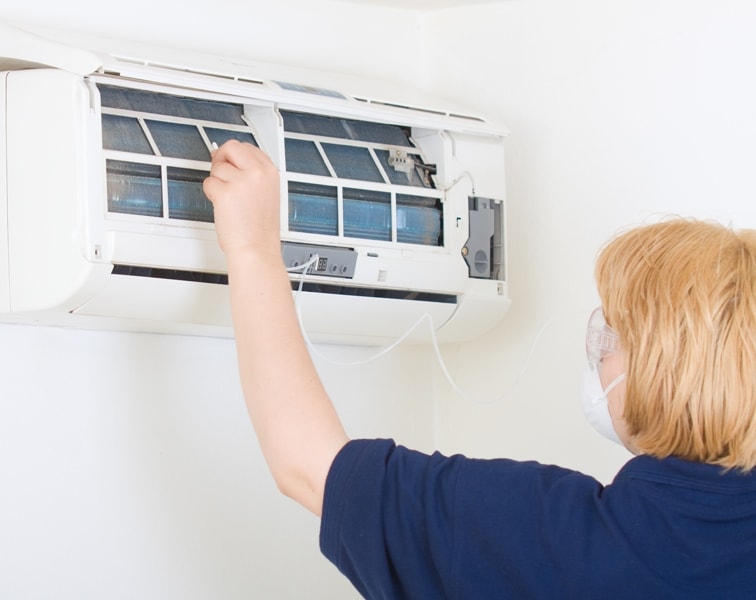 DUC_003-2-iStock-185076324 Woman checking unit to help maintain her ductless heating & cooling system