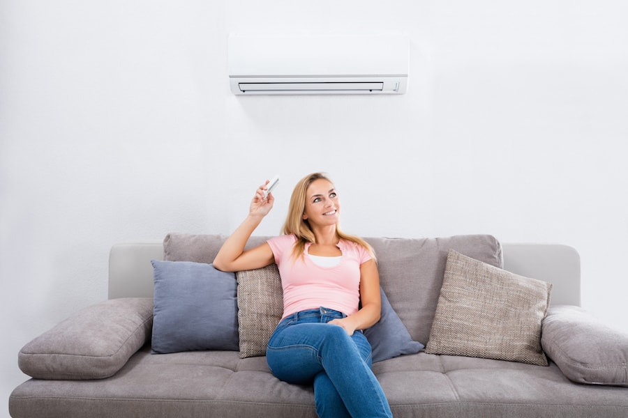 Happy woman operatinig a ductless AC unit while sitting on the couch.